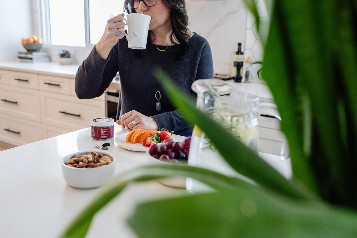 Jar of RELEVATE Brain Health Supplement on table with breakfast items and person drinking tea