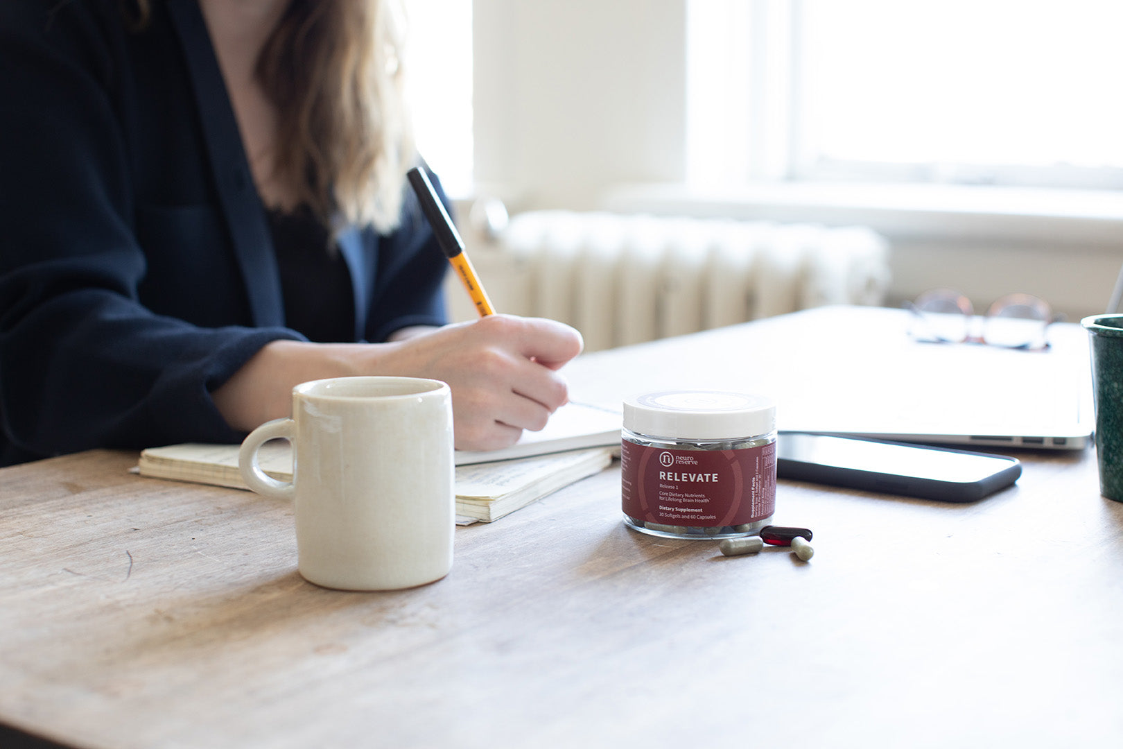 Jar of RELEVATE Brain Health Supplement on desk with woman working